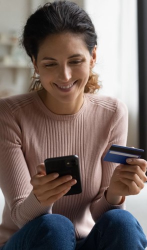 Woman smiling using her phone and holding her credit/debit card