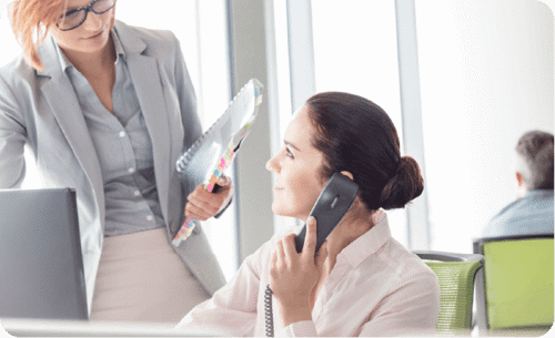 Woman on the phone with another woman standing over the desk
