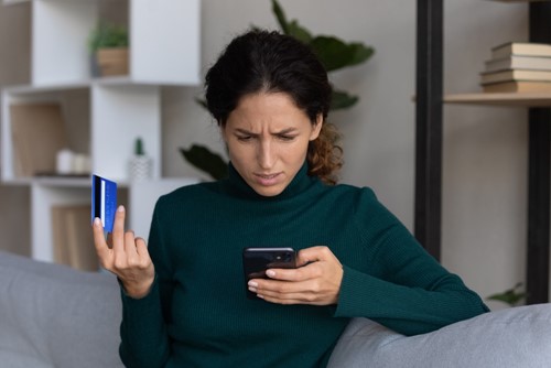 Woman looking confused at her phone with her card payment in other hand